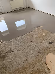 Boden mit einer sichtbaren Pfütze Wasser auf einer glatten Oberfläche neben einem rauen, beschädigten Bereich.