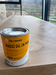 Dose mit Pallmann Magic Oil 2K Pure auf einem Holztisch vor einem Fenster.
