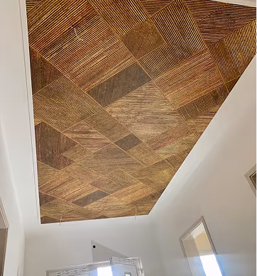 Decke mit einem geometrischen Muster aus Holzbrettern in verschiedenen Brauntönen in einem Hausflur.