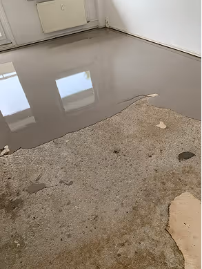 Boden eines Raums mit frisch aufgetragenem, glattem Nassestrich neben einem älteren, fleckigen Betonboden.