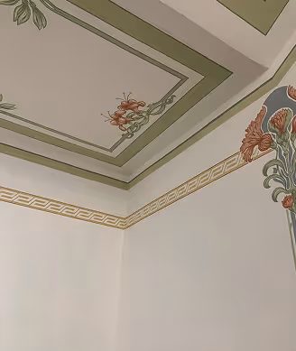 Decke und obere Wände mit grünen und goldenen dekorativen Bordüren und braunen floralen Mustern.