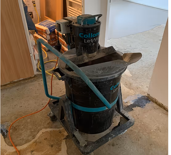 Schwarze Collomix Leichtmörtel-Maschine auf einem Baustellenboden mit angeschlossenen Kabeln.