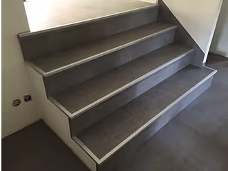 Graue Treppe mit Holzoptik und Metallkante in einem hellen Raum.